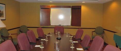 Un salón de conferencias con una larga mesa, sillas rojas y una pantalla para proyector.