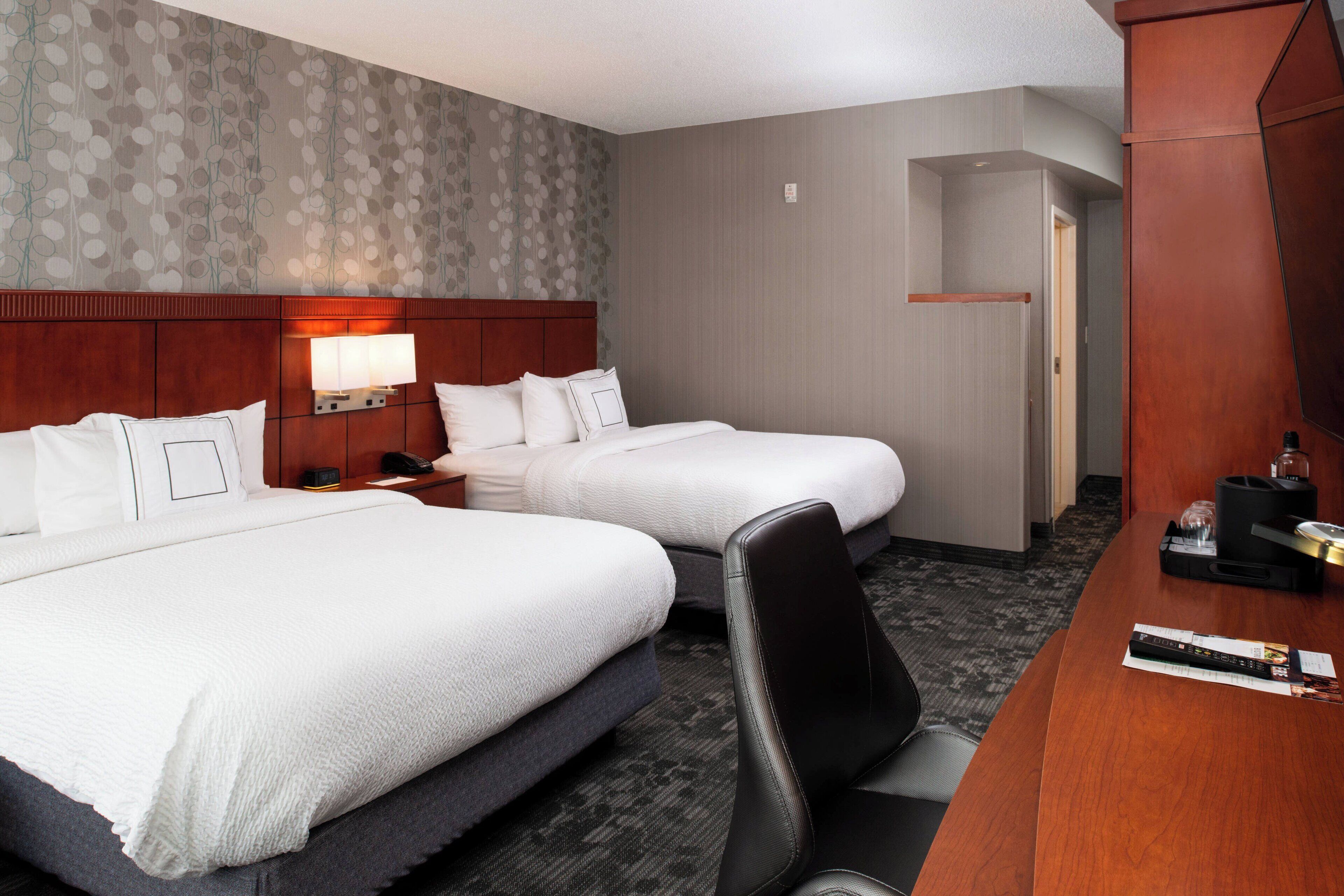 A hotel room with two beds, a desk with a chair, a lamp, and a minibar.