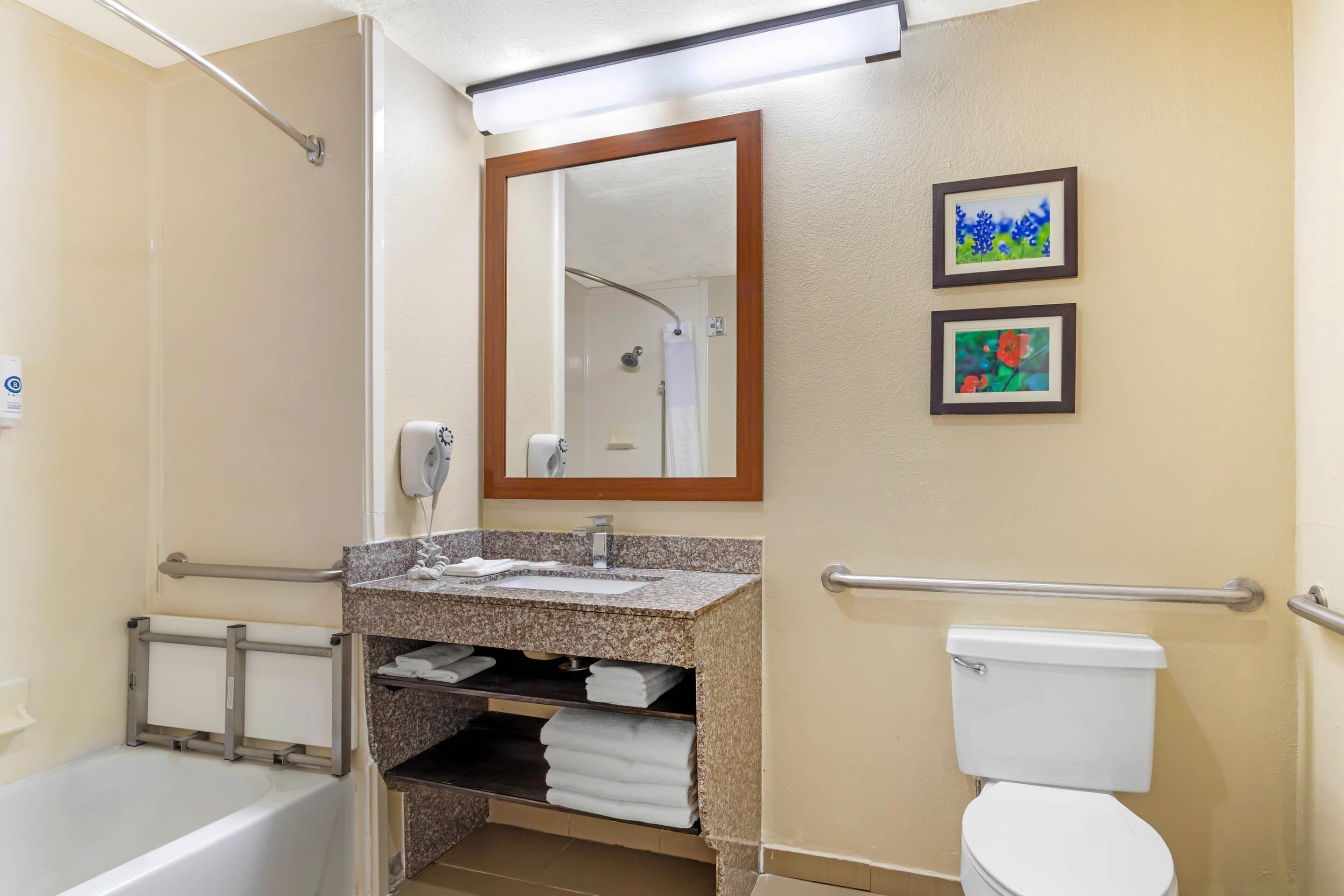 A bathroom with a bathtub, a sink with a mirror, a toilet, and two framed pictures on the wall.
