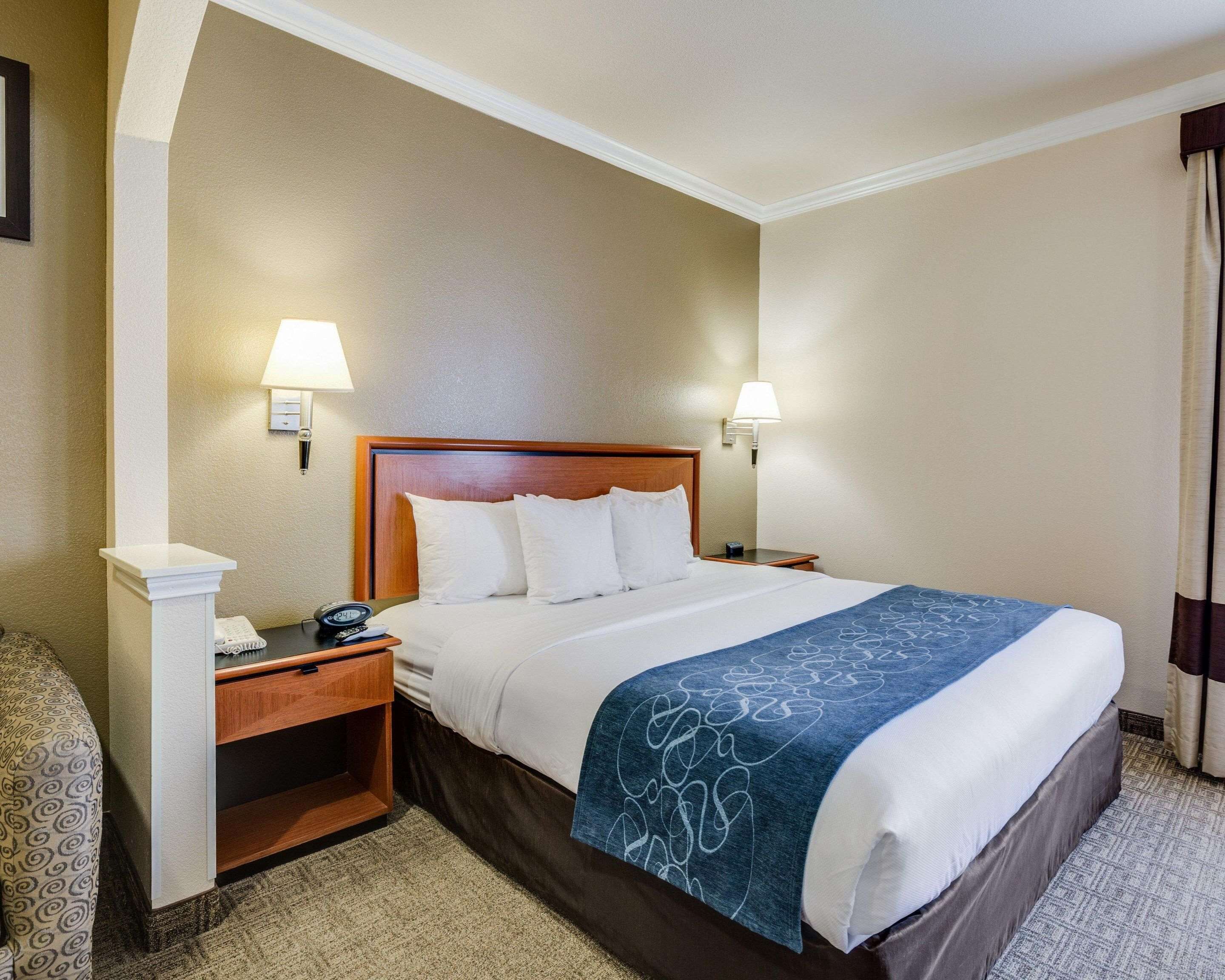 Une chambre d’hôtel avec un grand lit, deux lampes de chevet, une table de chevet avec un téléphone et une chaise à motifs.