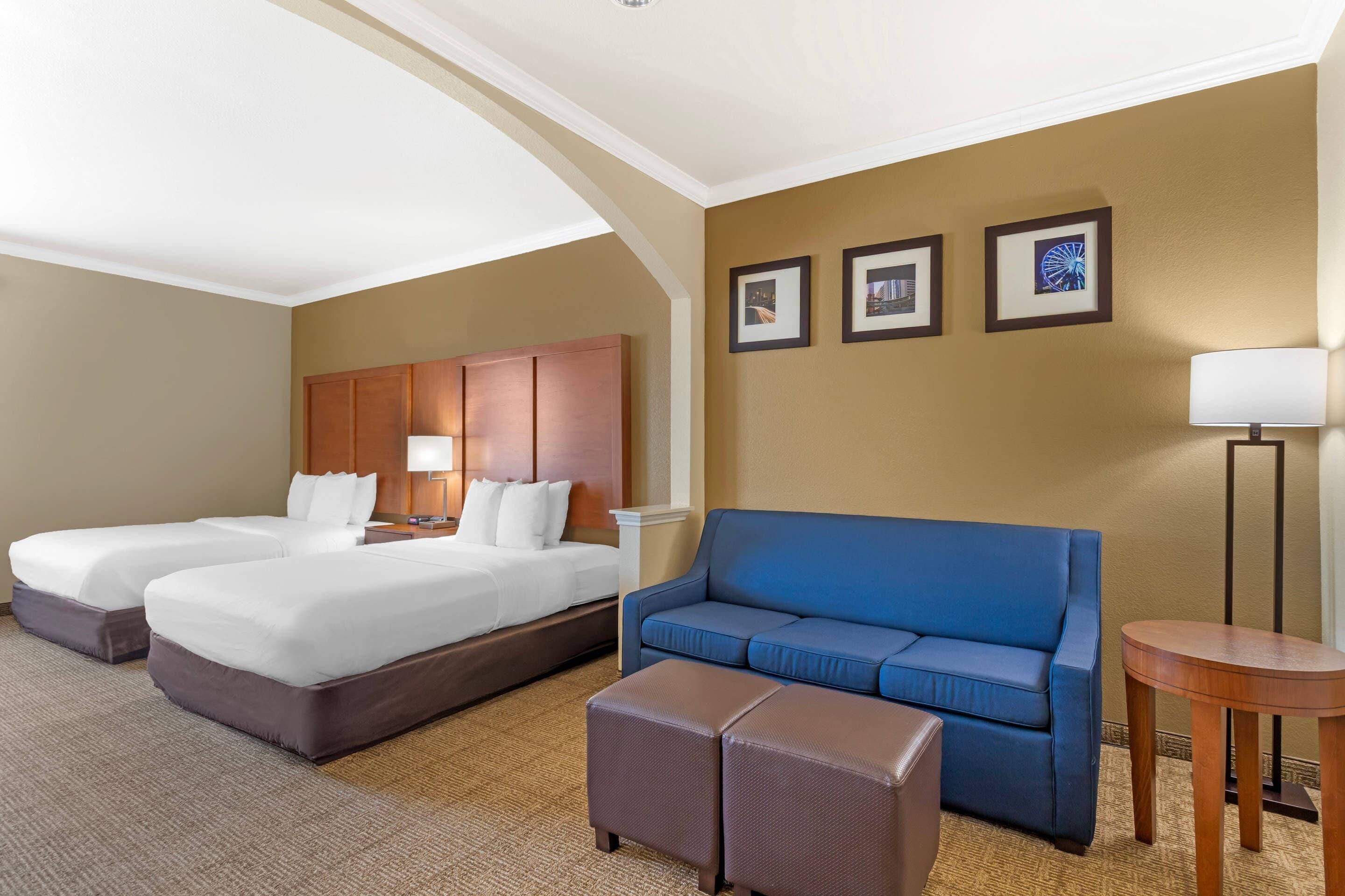 A hotel room with two beds, a blue sofa, a small table, and framed pictures on the wall.