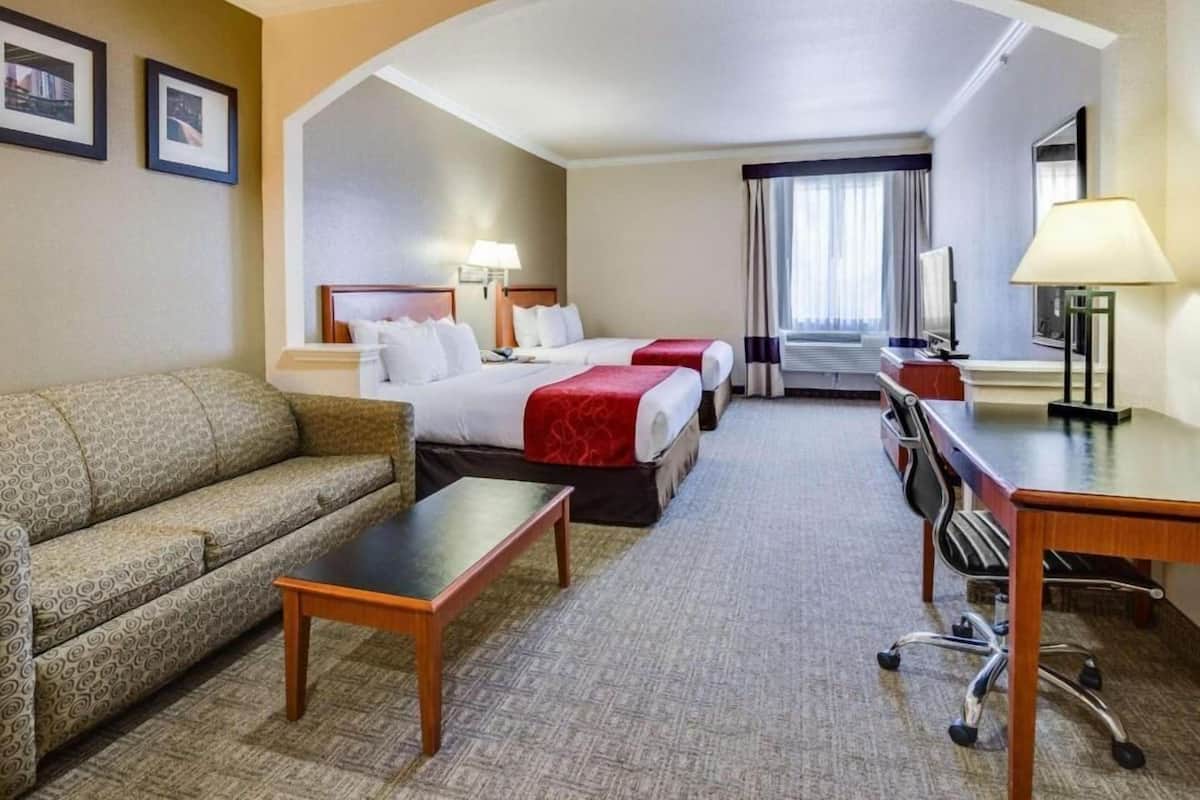 A hotel room with a sofa, two beds, a desk, a chair, and a TV.