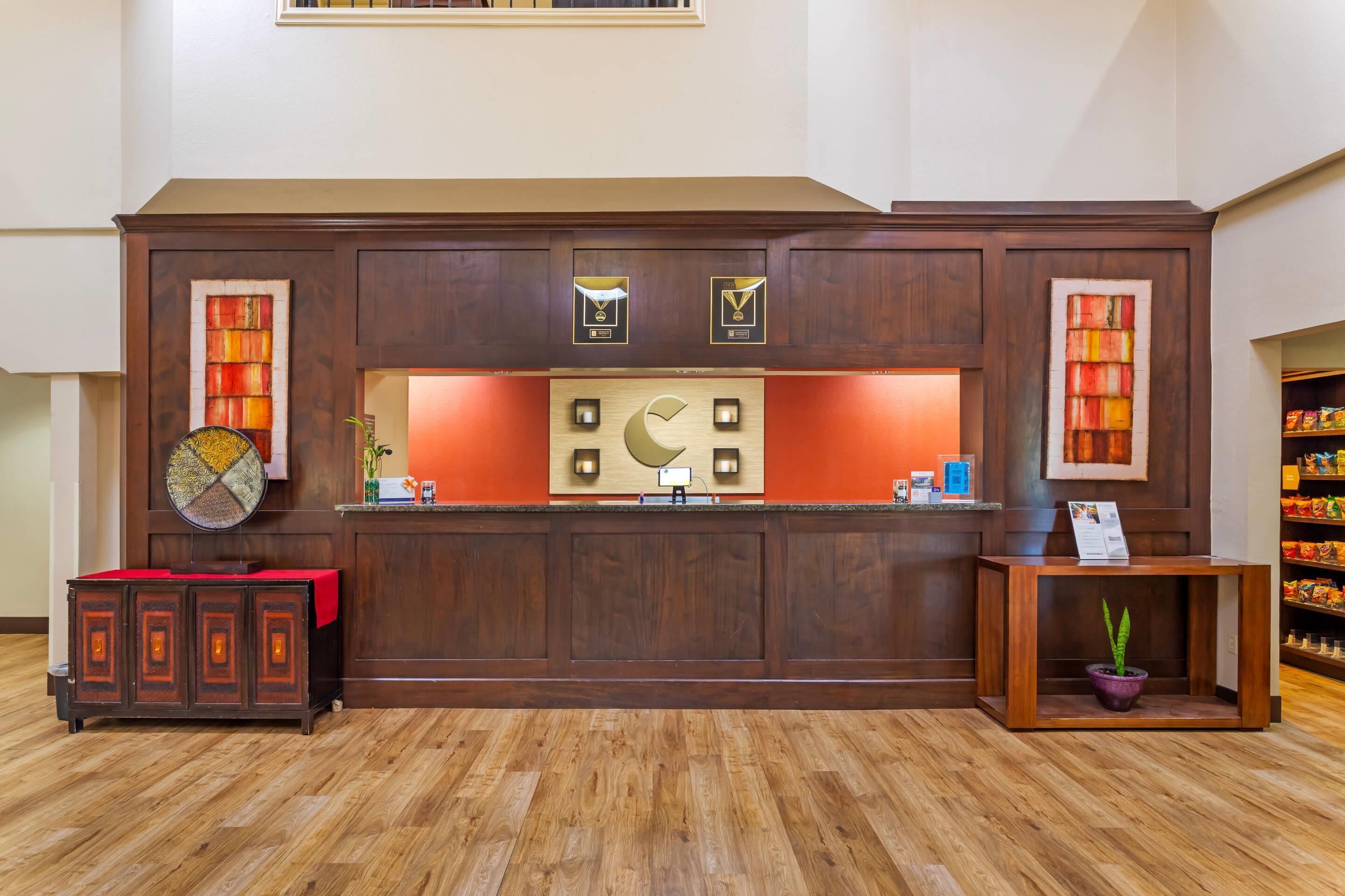 A reception desk with a wooden finish, a potted plant, and a small table with a sign.