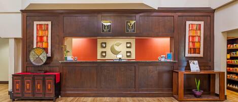 A reception desk with a wooden finish, a potted plant, and a small table with a sign.