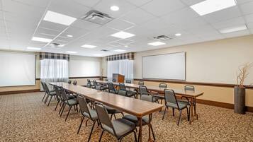 Un salón de conferencias con una larga mesa, sillas, una pantalla de proyector y piso alfombrado.