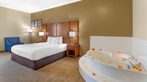 A hotel room with a bed, a blue chair, a nightstand with lamps, and a bathtub with flower petals. - Comfort Suites Deer Park Pasadena (Deer Park)