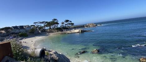 A coastal view with clear waters, a sandy beach, and a rocky shoreline.