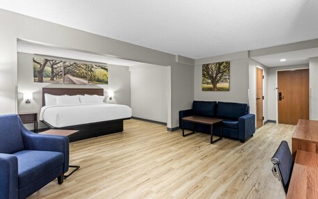 A hotel room with a bed, a blue sofa, a wooden coffee table, and a wooden door.