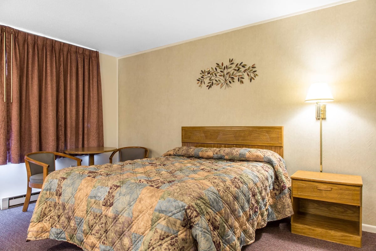 A hotel room with a bed, a wooden nightstand, a desk, and a chair.
