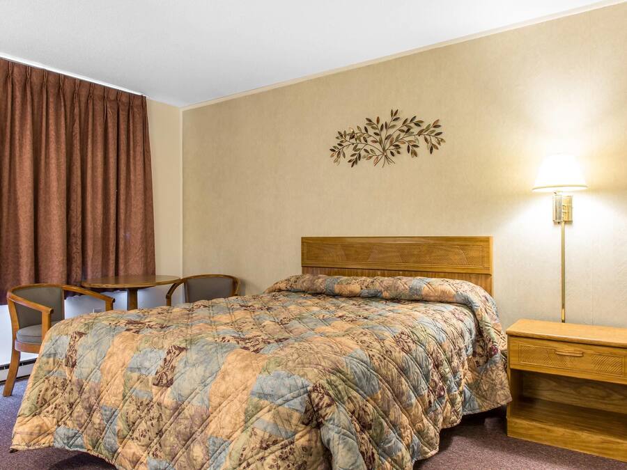 A hotel room with a bed, a wooden nightstand, a desk, and a chair.