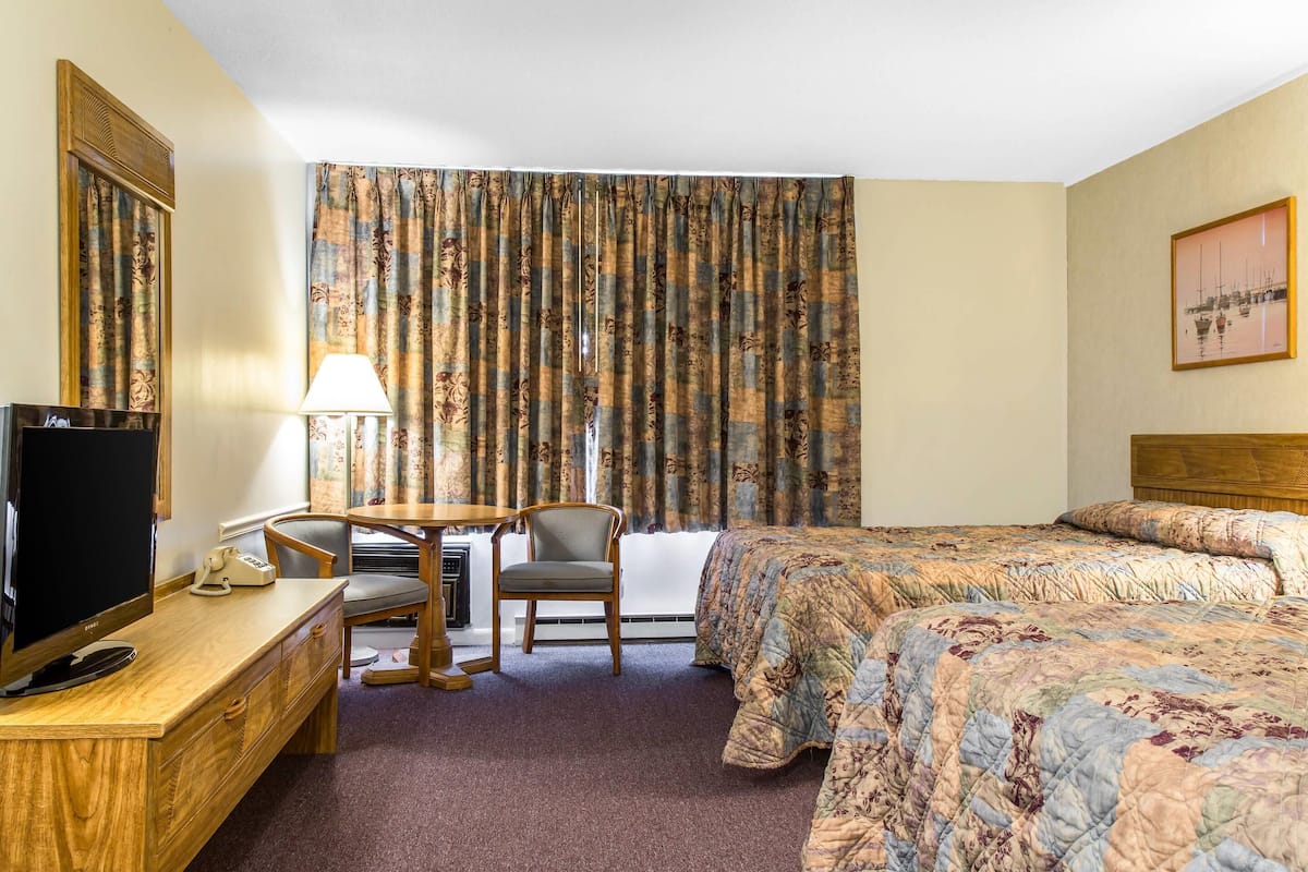 A hotel room with a bed, a desk with a TV, a chair, a lamp, and curtains.