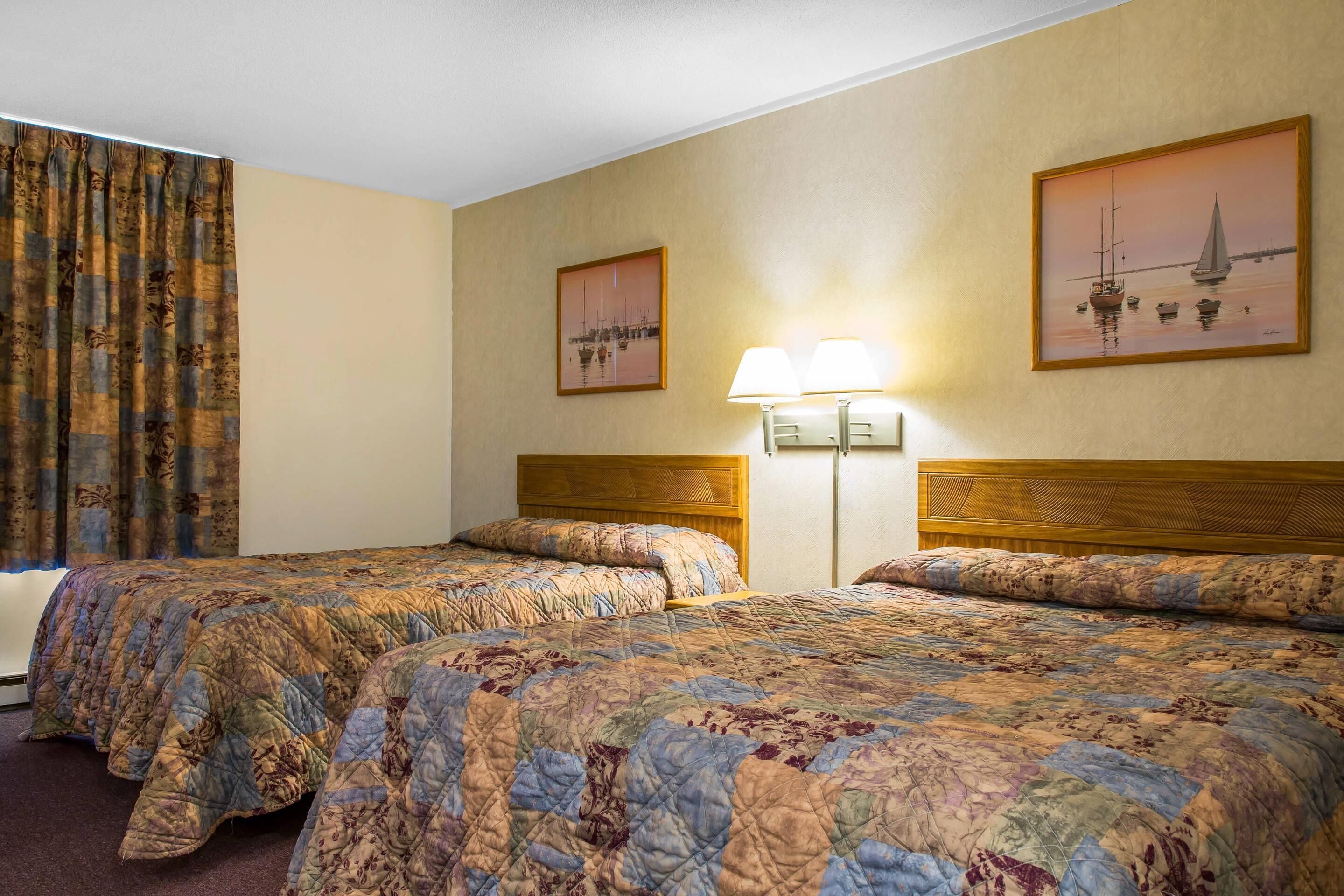 A hotel room with two beds, a window with curtains, and two wall-mounted lamps.