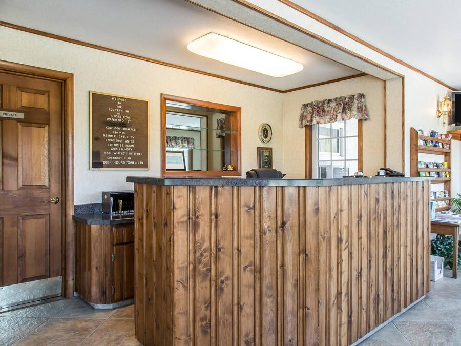 A reception area with a wooden reception desk, a private door, a mirror, a clock, a television, and a bookshelf.