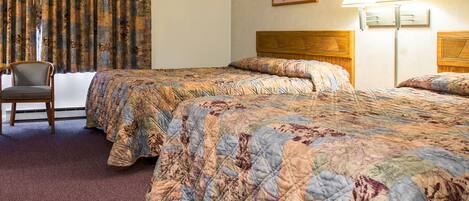 A hotel room with two beds, a chair, a lamp, and a painting on the wall.