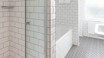 Un baño moderno con azulejos blancos tipo metro, cabina de ducha de vidrio, bañera y suelo con estampado geométrico.