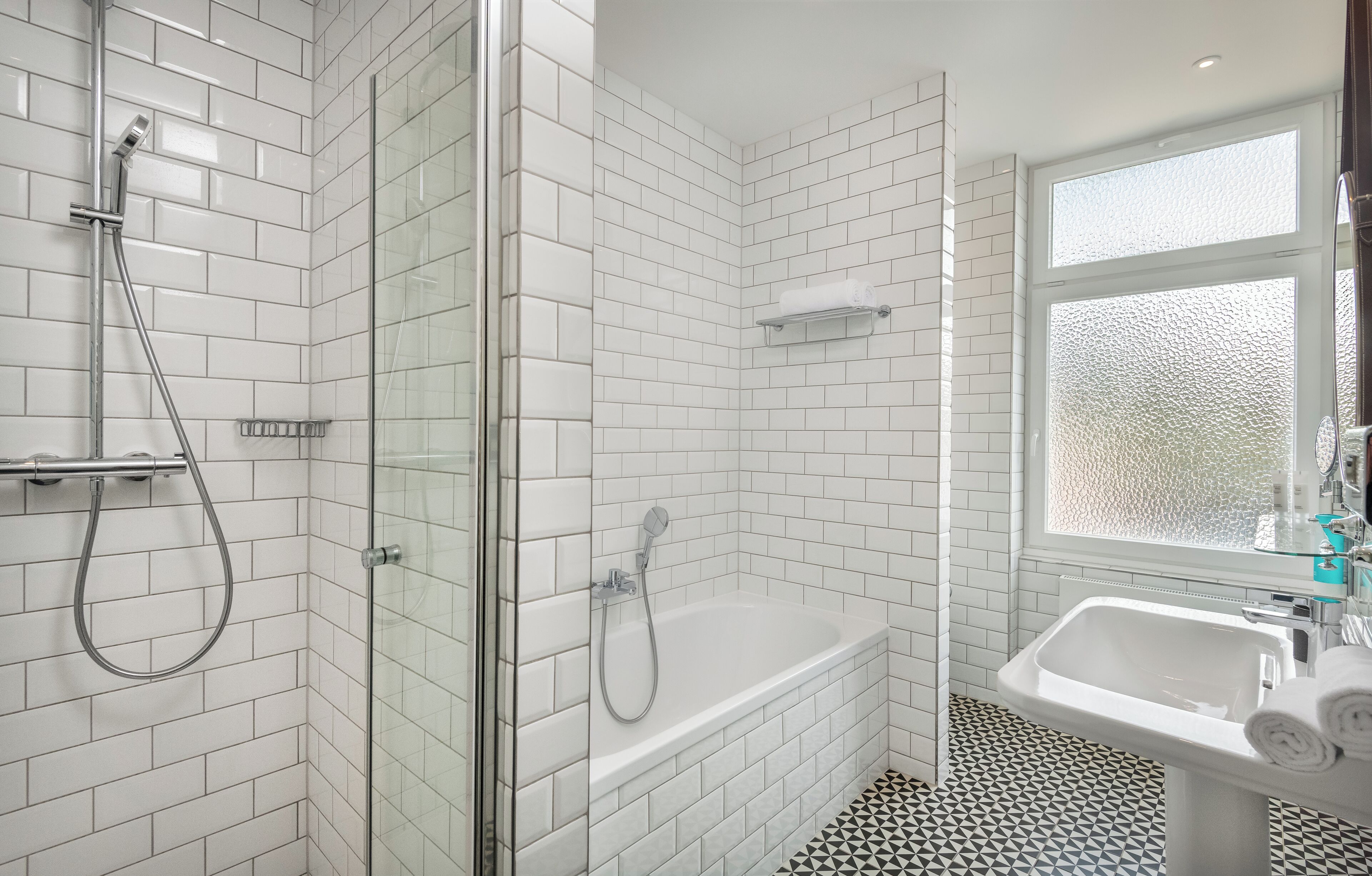 A bathroom with white subway tiles, a glass shower enclosure, a white bathtub, and a sink with a mirror.
