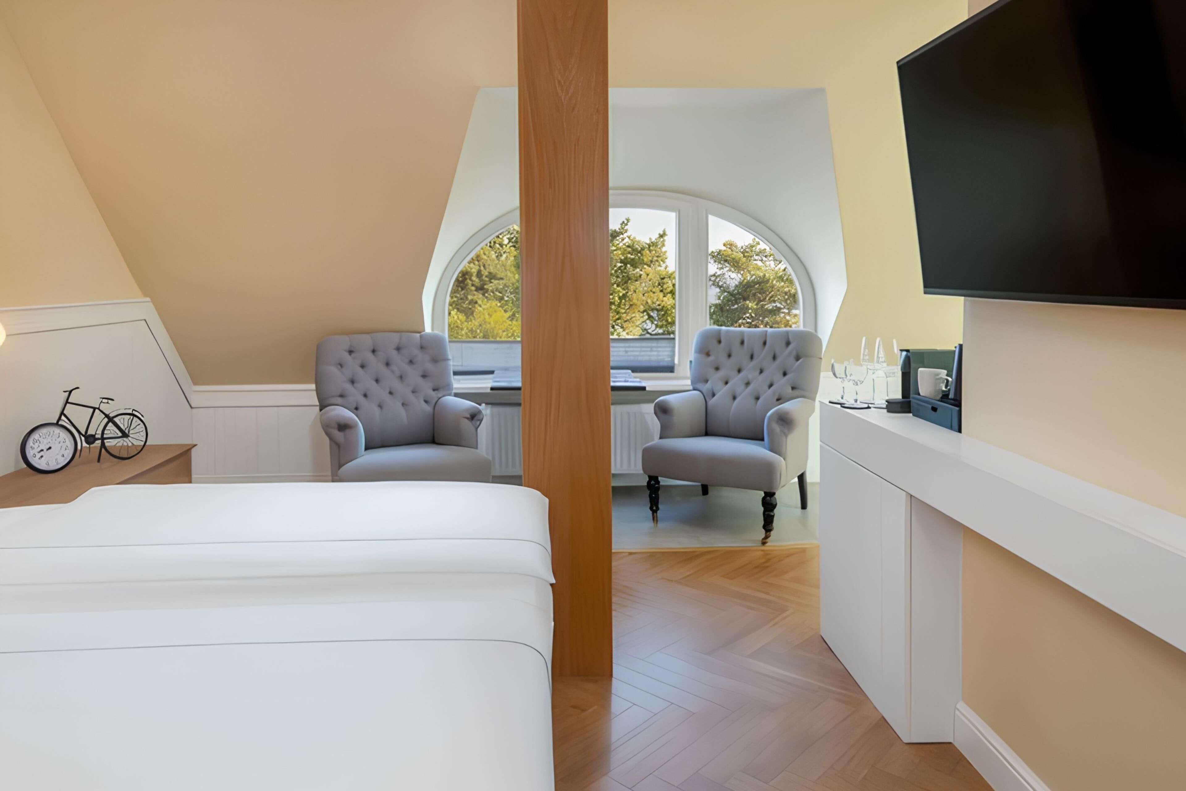 A bedroom with a bed, two armchairs, a wooden column, a TV, and a window with a view.