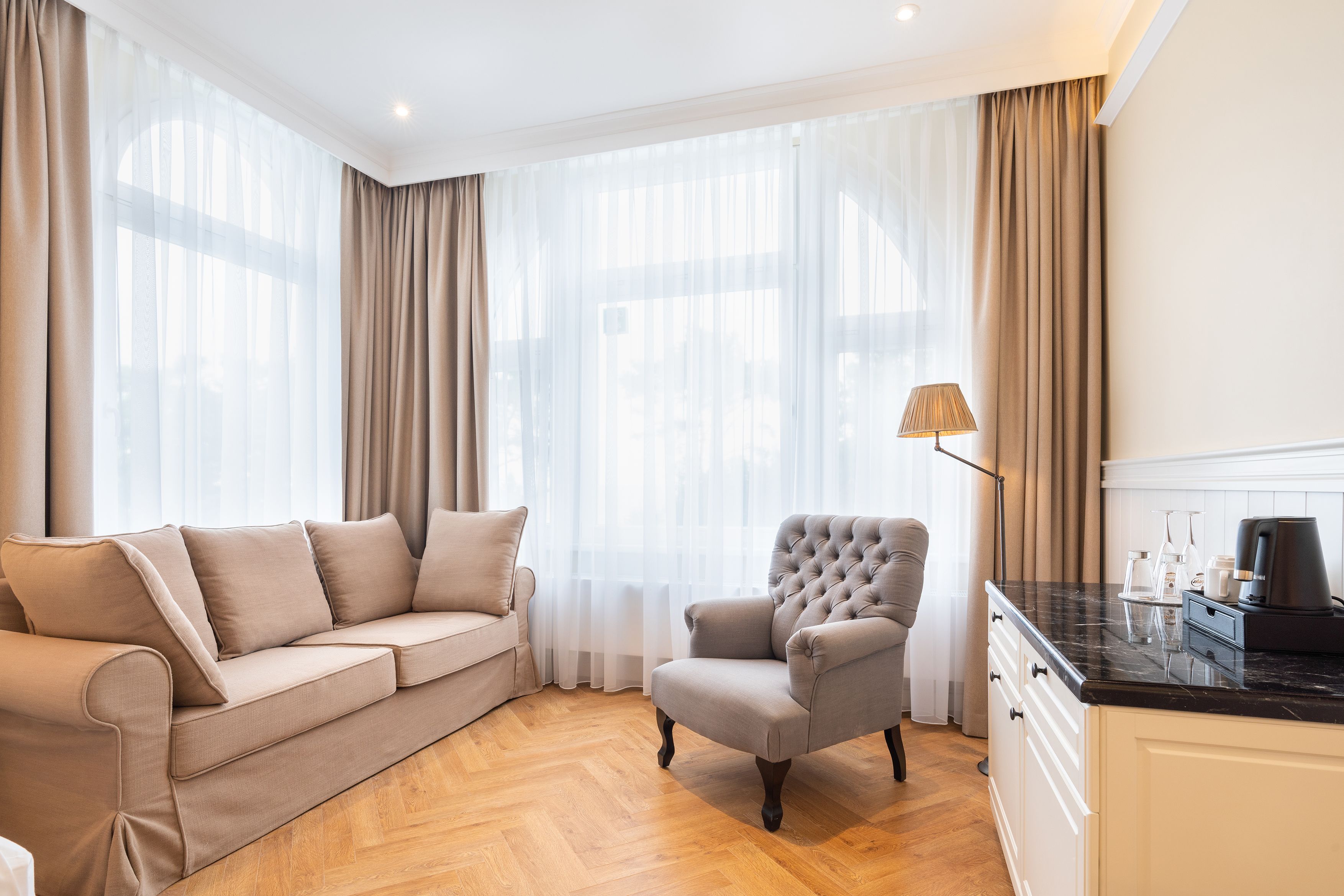 Een moderne woonkamer met een beige bank, een gestoffeerde fauteuil en een koffiezetapparaat op een marmeren aanrecht.