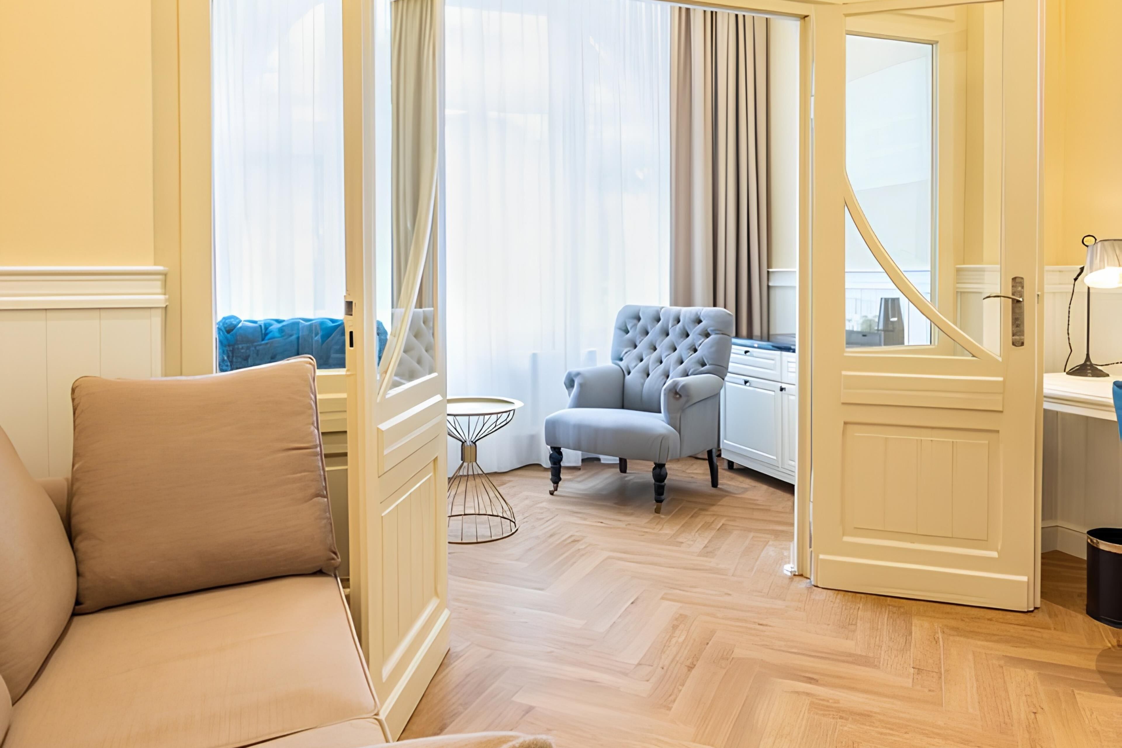 A hotel room with a sofa, a chair, a small table, and a door leading to another room.
