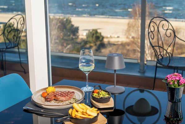 A dining table with a plate of food, a glass of white wine, and a vase of flowers. - Strandhotel Ahlbeck, a member of Radisson Individuals (Heringsdorf)