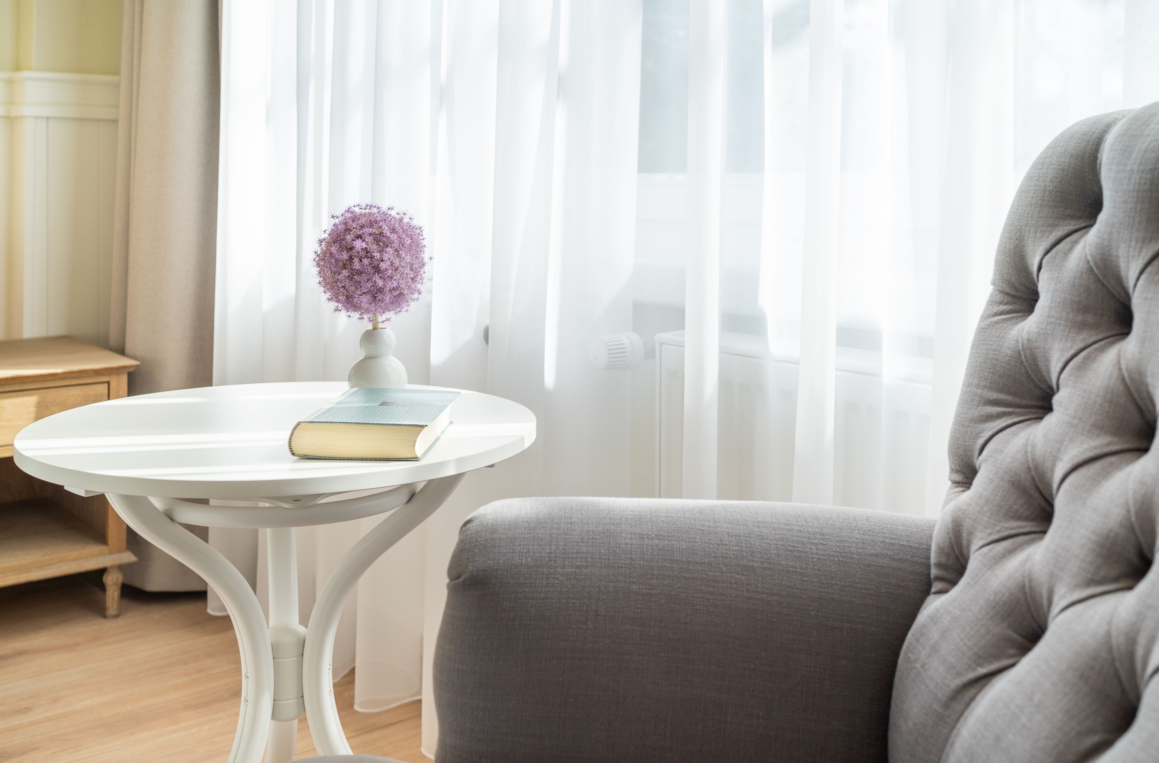 A room with a round white table, a grey upholstered armchair, and a white radiator.