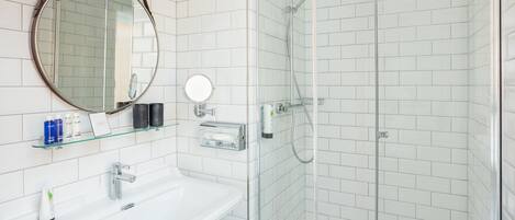 Ein modernes Badezimmer mit einem weißen Waschbecken, einem runden Spiegel und einer Dusche mit Glaswand.