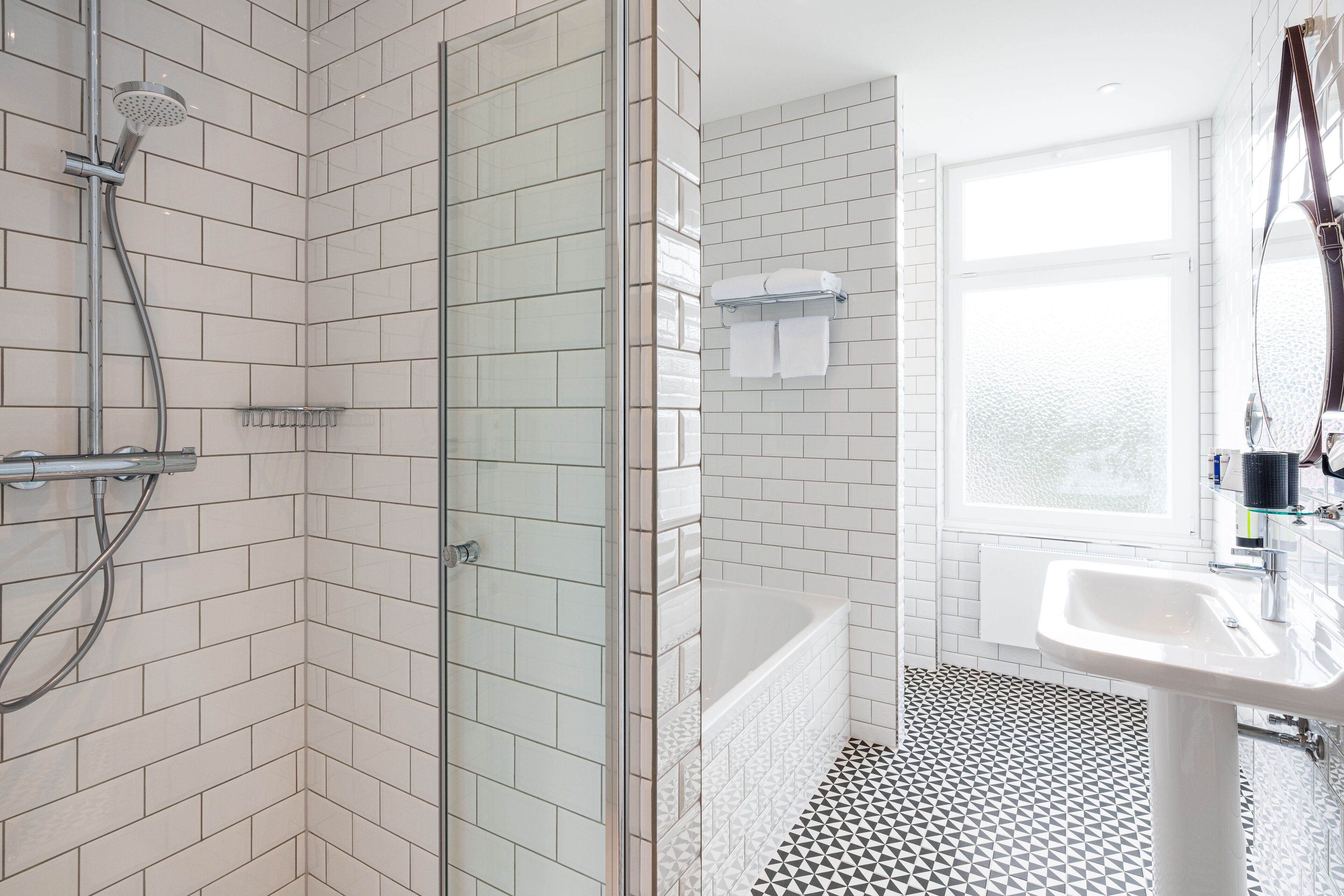 A modern bathroom with a glass-enclosed shower, a white bathtub, and a sink with a mirror.