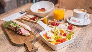 Disposição para o pequeno-almoço com sanduíche, salada de fruta, café e sumo numa mesa de madeira.