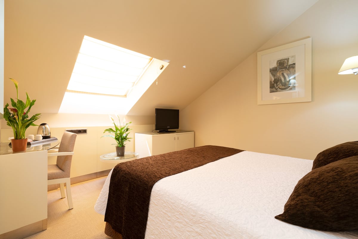 A bedroom with a bed, a desk, a chair, a television, and a window.
