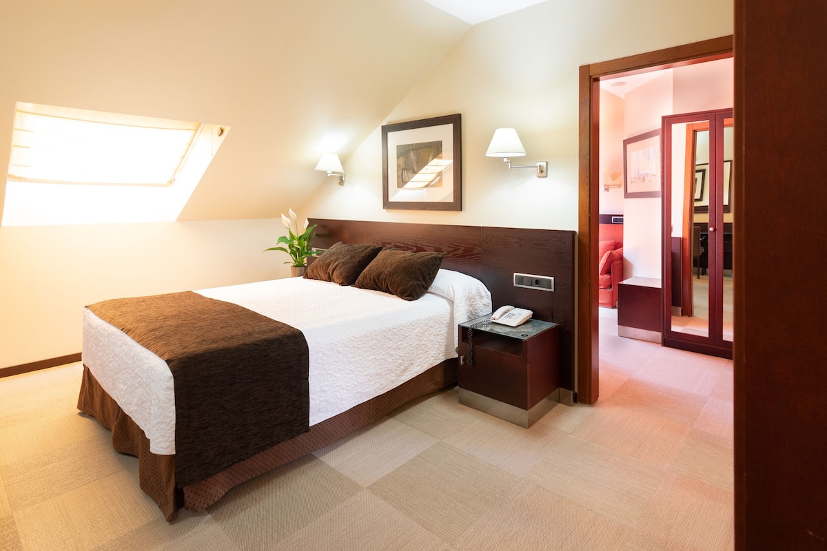 A hotel room with a bed, bedside table, lamp, and a framed picture on the wall.