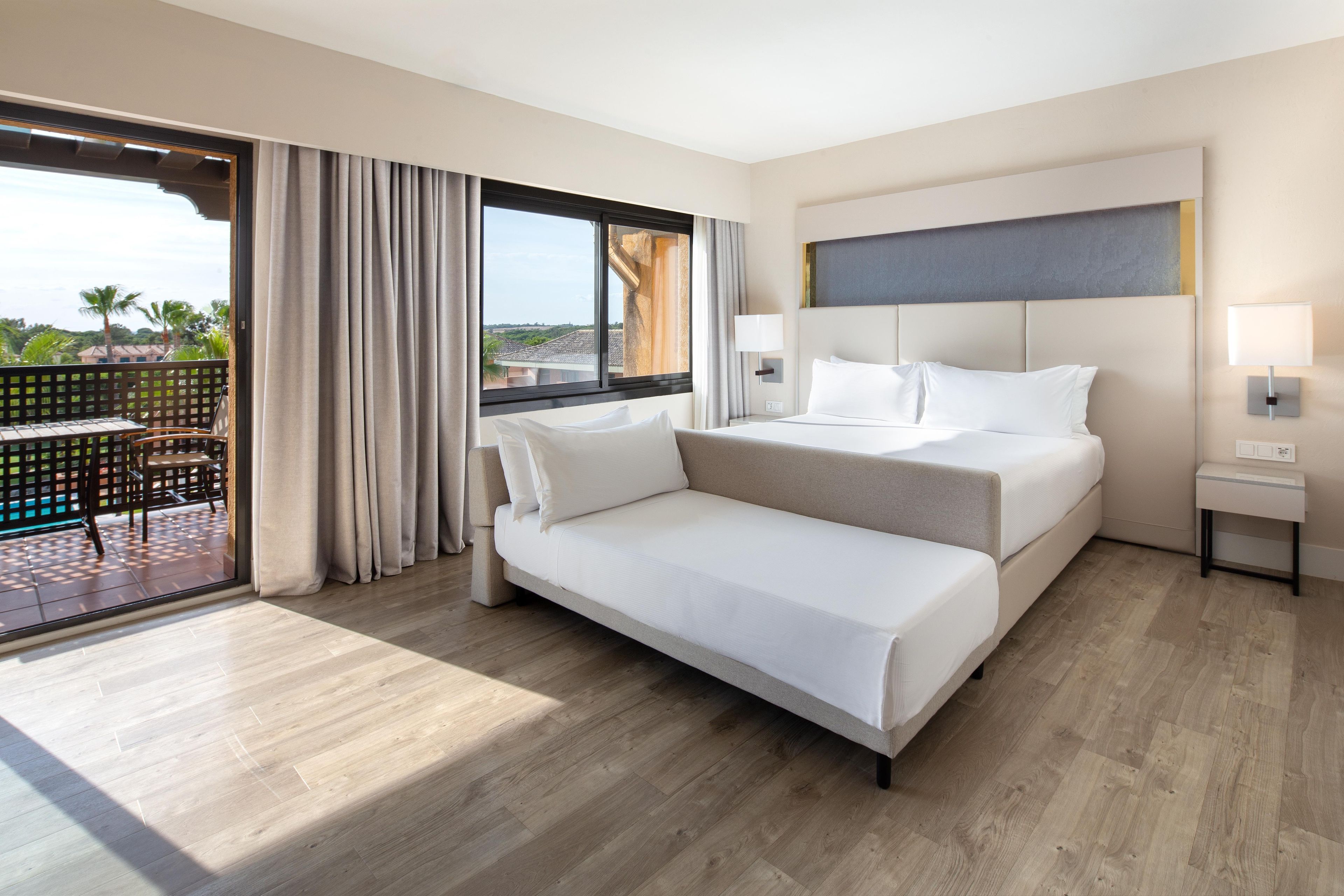 A hotel room with a bed, a desk, and a view of palm trees.