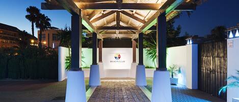 Entrada techada a un club de playa, con logotipo, columnas y suelo estampado.