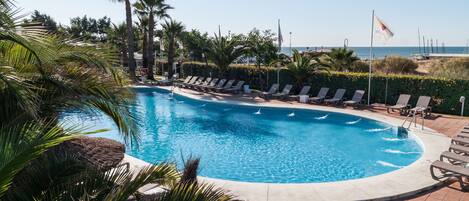 Una piscina con sillones de descanso y palmeras.