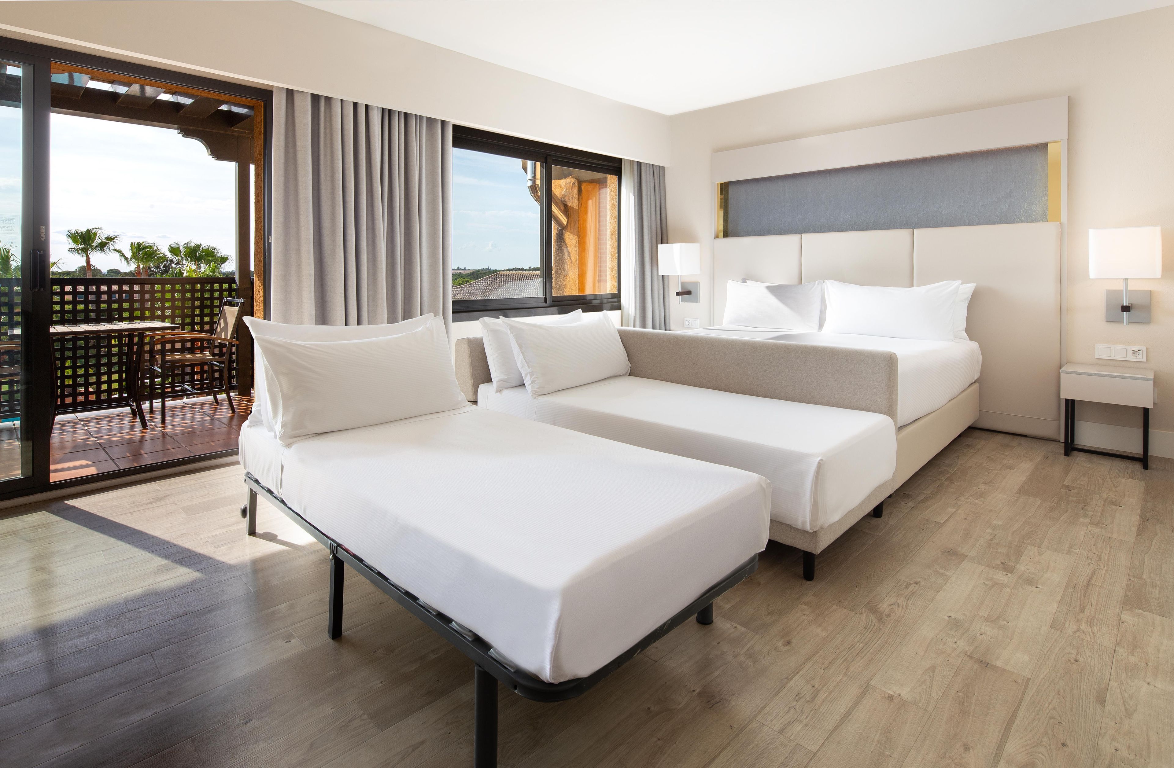 A hotel room with two beds, a balcony, and a view of palm trees.