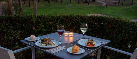 A dining table set outdoors with plates of food, glasses, and candles.