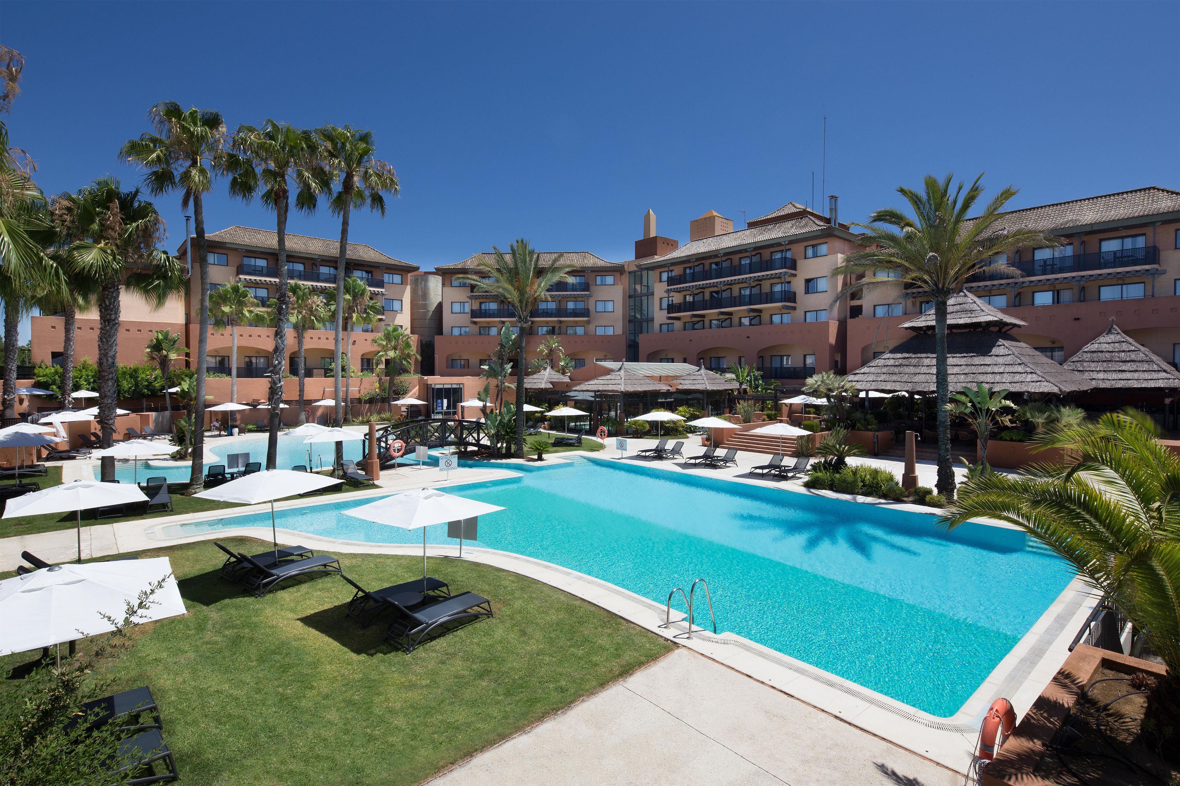 Un hôtel doté d’une piscine entour ée de palmiers et de chaises longues.