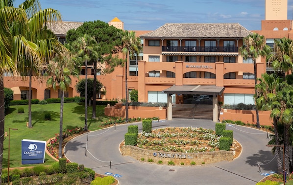 Un hotel DoubleTree by Hilton con una entrada ajardinada, un camino de acceso curvo y cielo despejado.