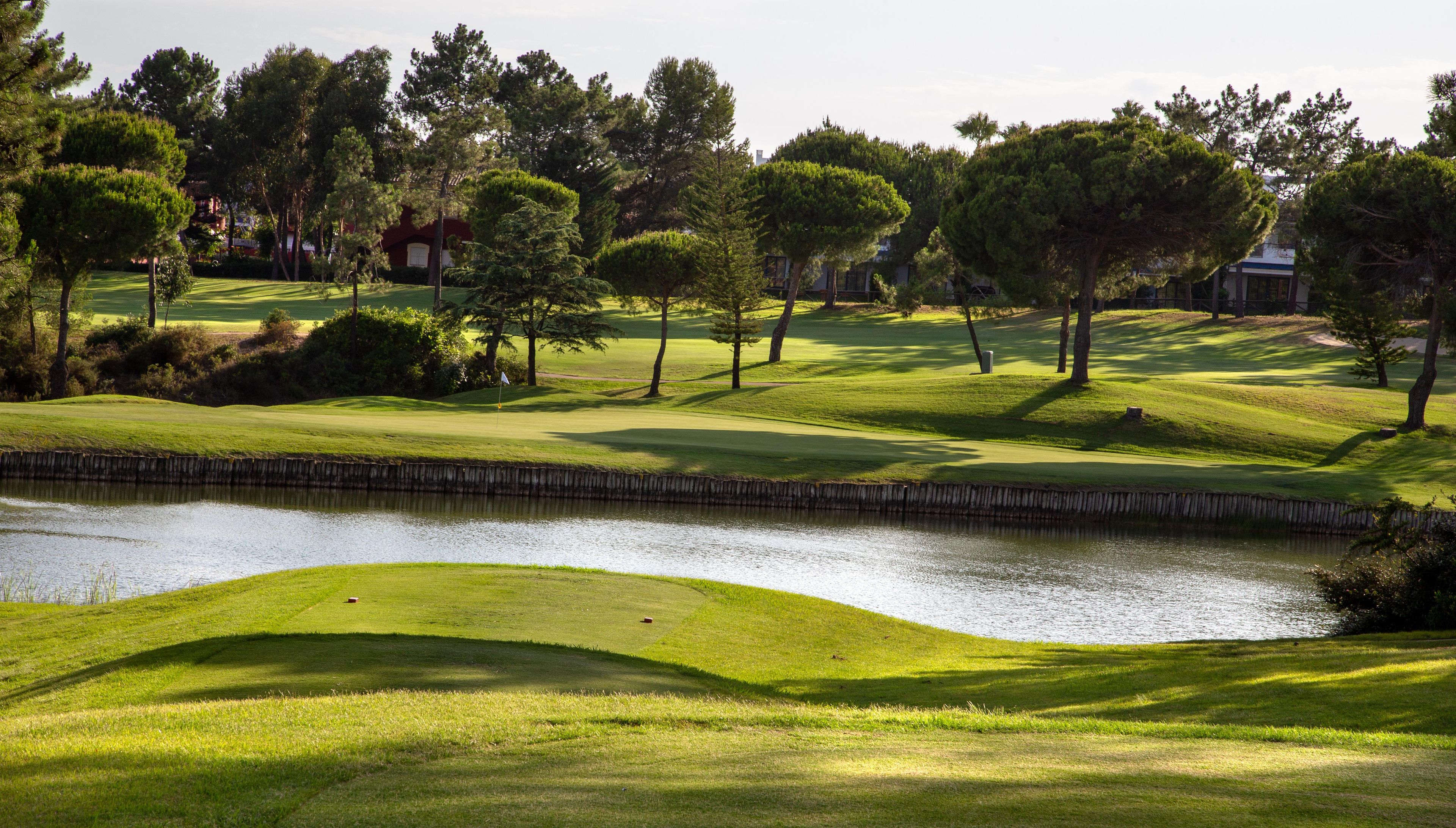 A golf course with a pond, trees, and a building in the background.