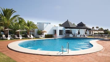 A pool area with lounge chairs, a sign reading 'Beach Club,' and a building with a modern design.