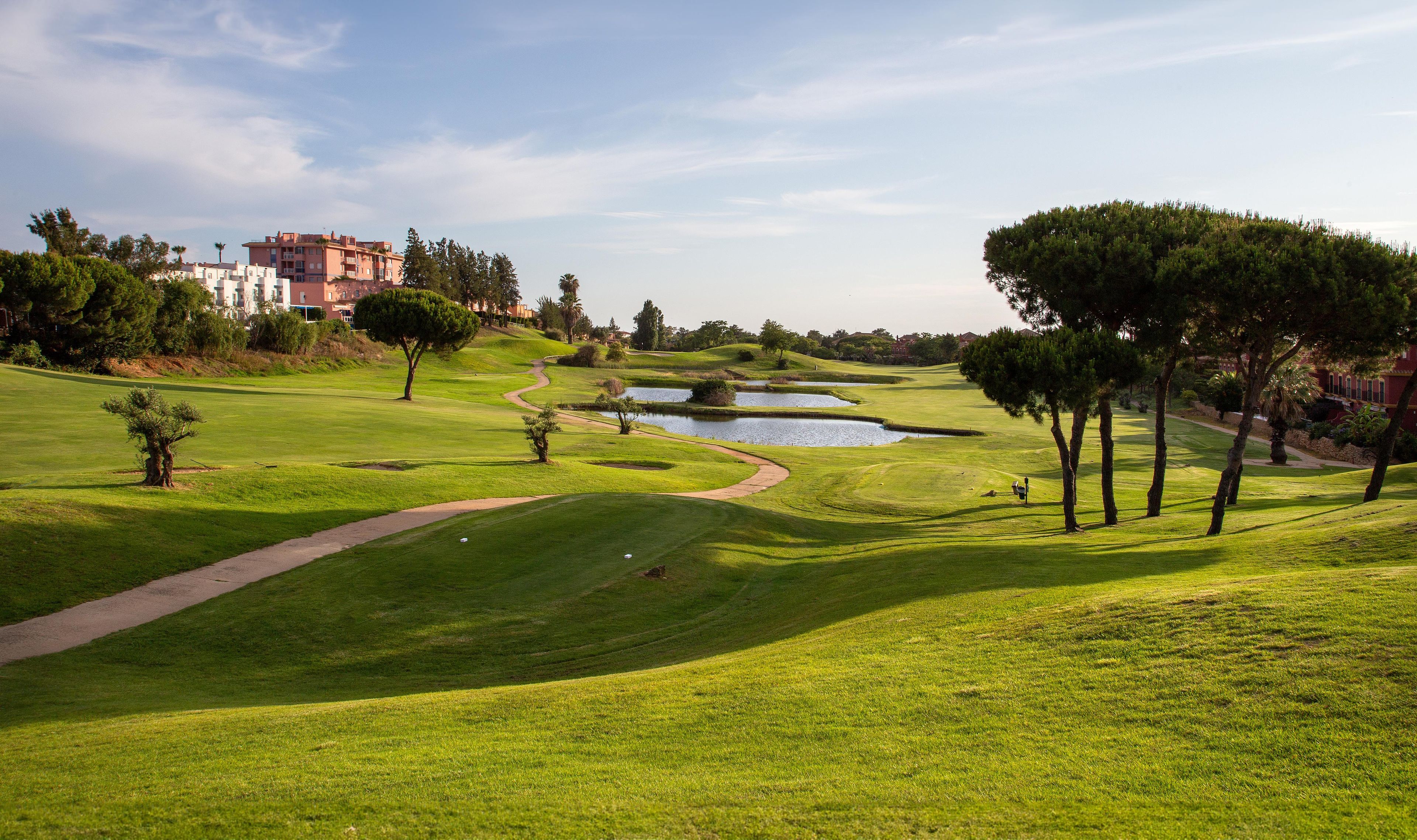 Un parcours de golf avec un étang, des arbres et un bâtiment en arrière-plan.