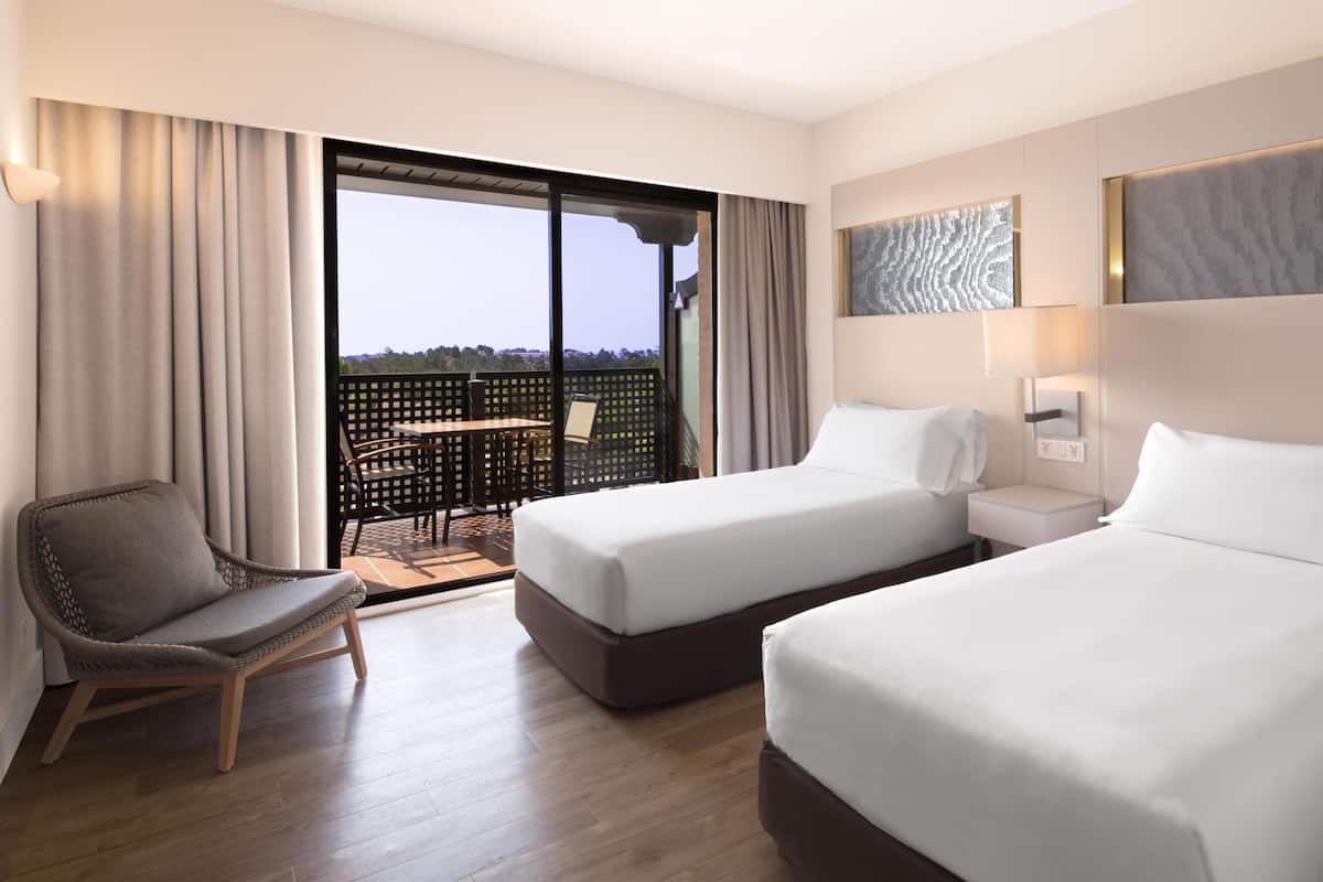 Ein Hotelzimmer mit zwei Betten, einem Sessel, einem kleinen Tisch und einem Balkon mit Blick.