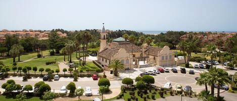 A hotel with a central courtyard, palm trees, and a view of the sea.