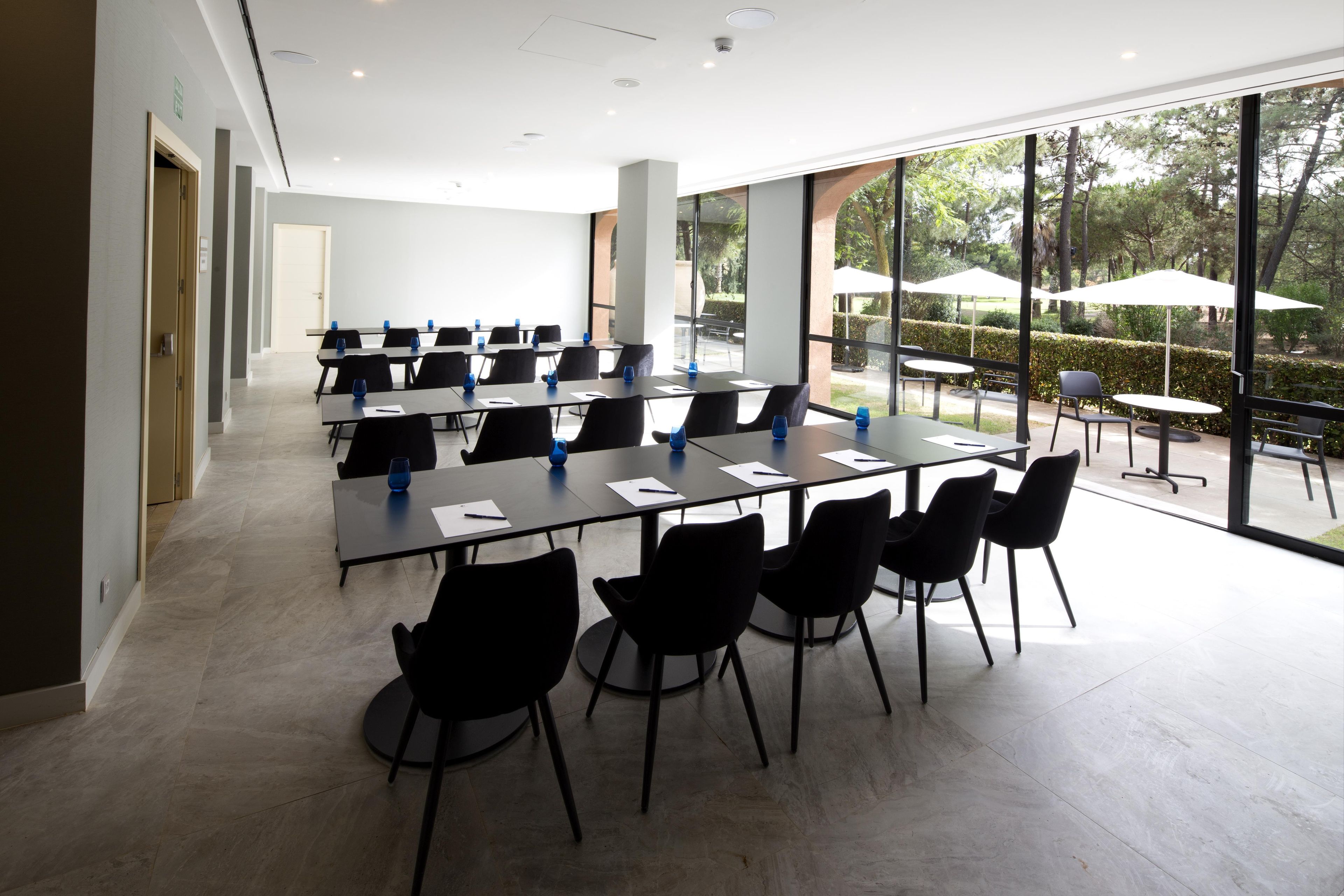 A conference room with tables and chairs, large windows, and a view of the outdoors.