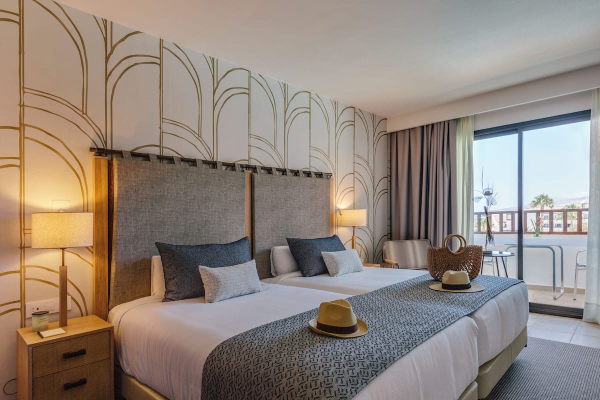 A hotel room with a large bed, two bedside tables, a nightstand, a balcony with a view, and a patterned wall.