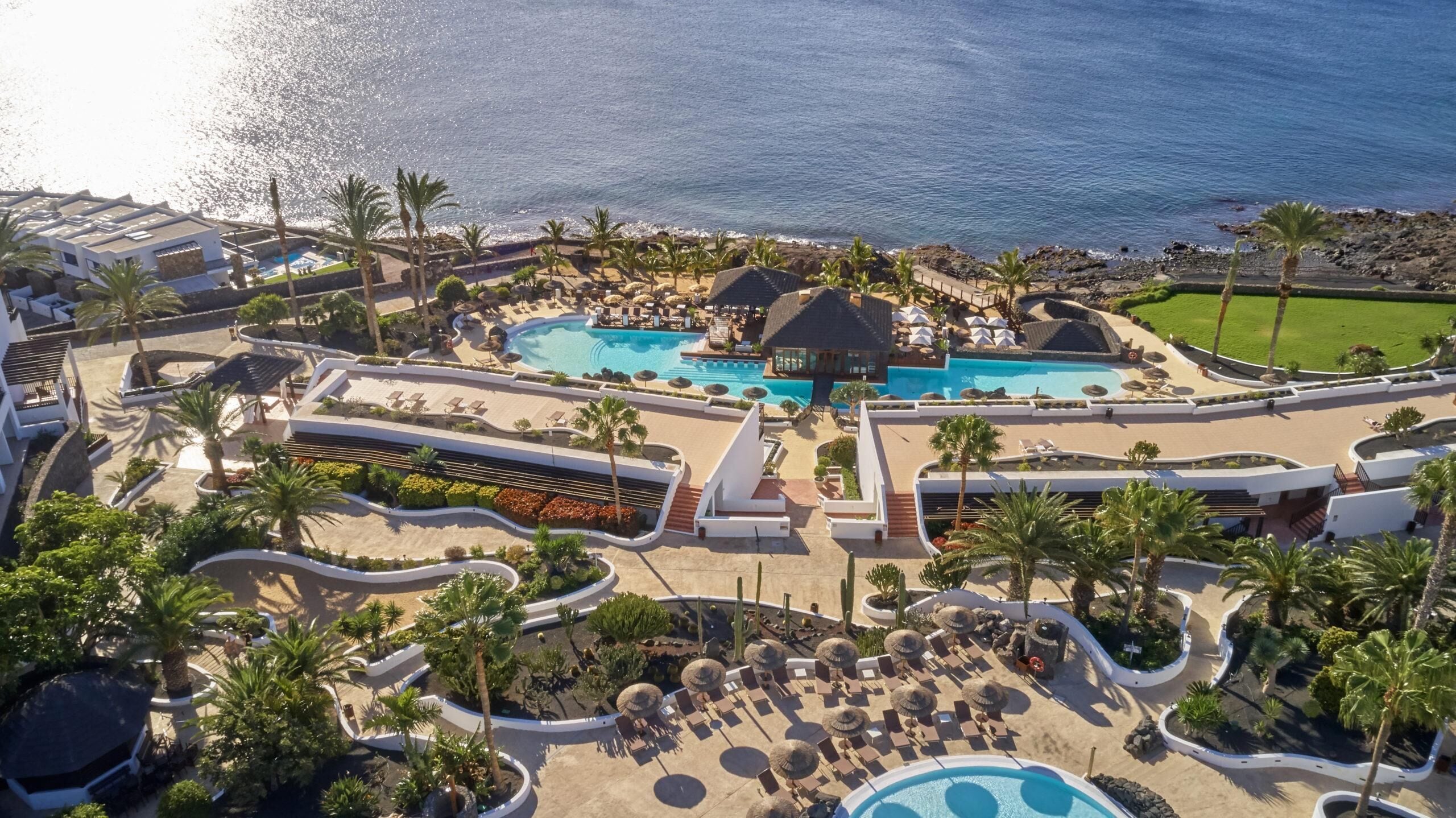 Vista aérea de un resort con múltiples piscinas, palmeras y zonas de descanso.