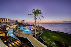 A resort with a swimming pool, palm trees, and a view of the ocean at dusk. - Secrets Lanzarote Resort & Spa - Adults Only (+18) - Hyatt Inclusive Collection (Yaiza)