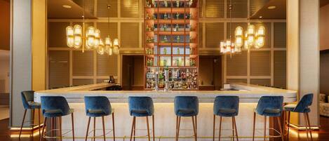 A bar area with a central counter, multiple bar stools, and shelves stocked with bottles.