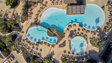 Vista aérea de un complejo turístico con varias piscinas, tumbonas y palmeras.