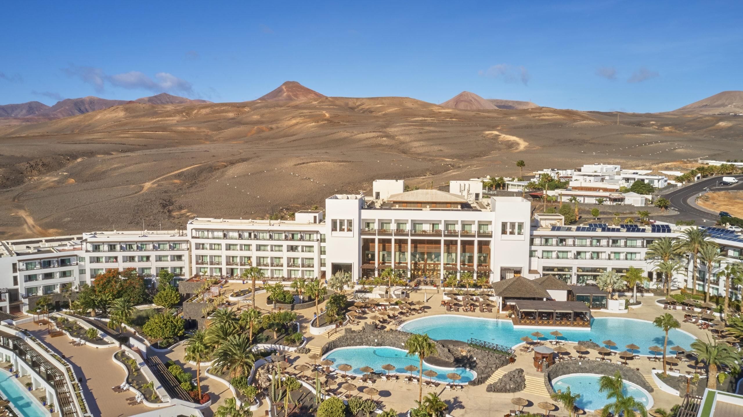 Um resort com várias piscinas, um edifício central com varandas e um cenário montanhoso ao fundo.