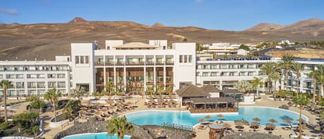 Un resort con varias piscinas, un edificio grande con balcones y un paisaje montañoso de fondo.